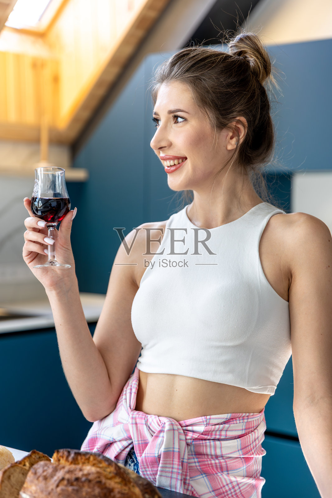 女人在厨房里微笑着，手里拿着一杯红酒。愉悦的片刻。照片摄影图片