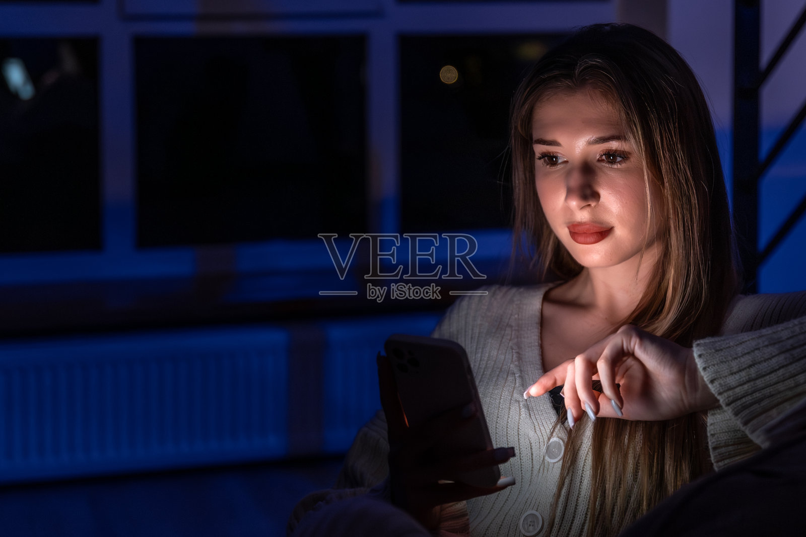 年轻女子在窗边轻触智能手机屏幕，深夜触屏。照片摄影图片