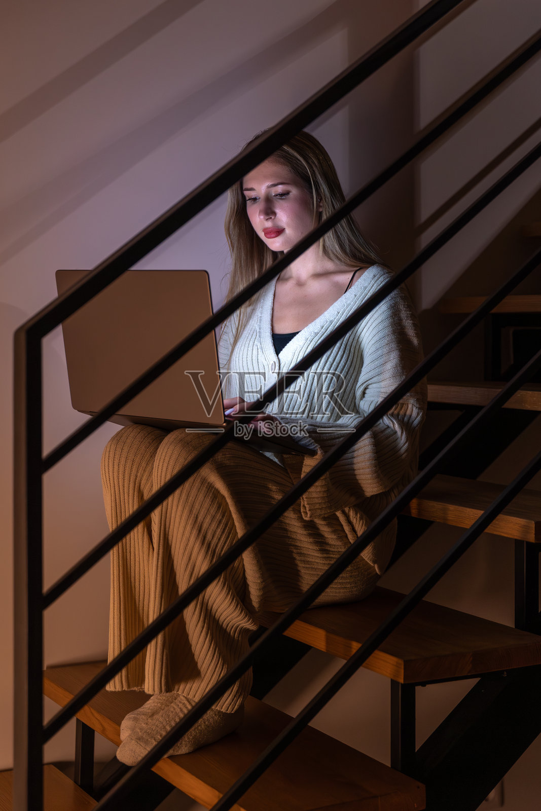 年轻女子在楼梯上，在宁静的居家氛围中观看笔记本电脑屏幕。晚间焦点。照片摄影图片