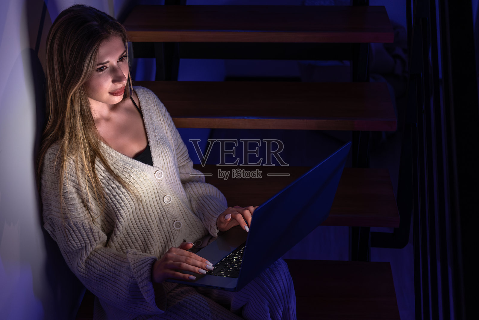 夜间在楼梯上用笔记本电脑工作的年轻女子。宁静的家庭办公室。照片摄影图片