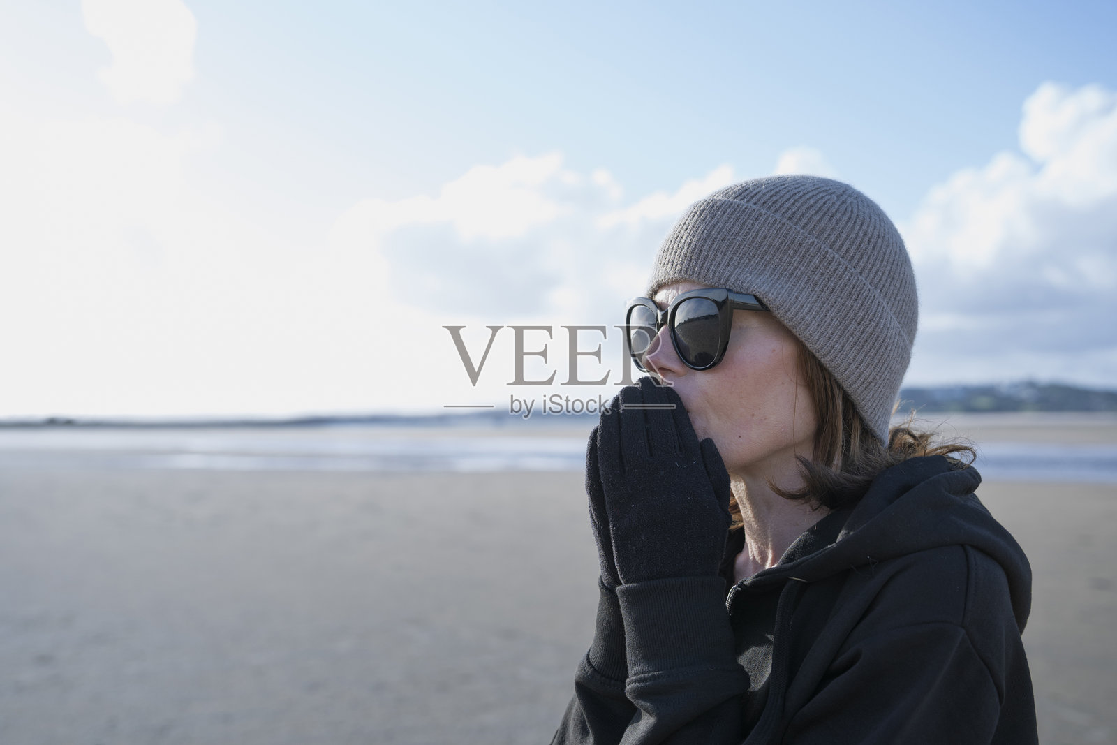 寒冷天气里，一名女子对着戴着手套的手哈气照片摄影图片