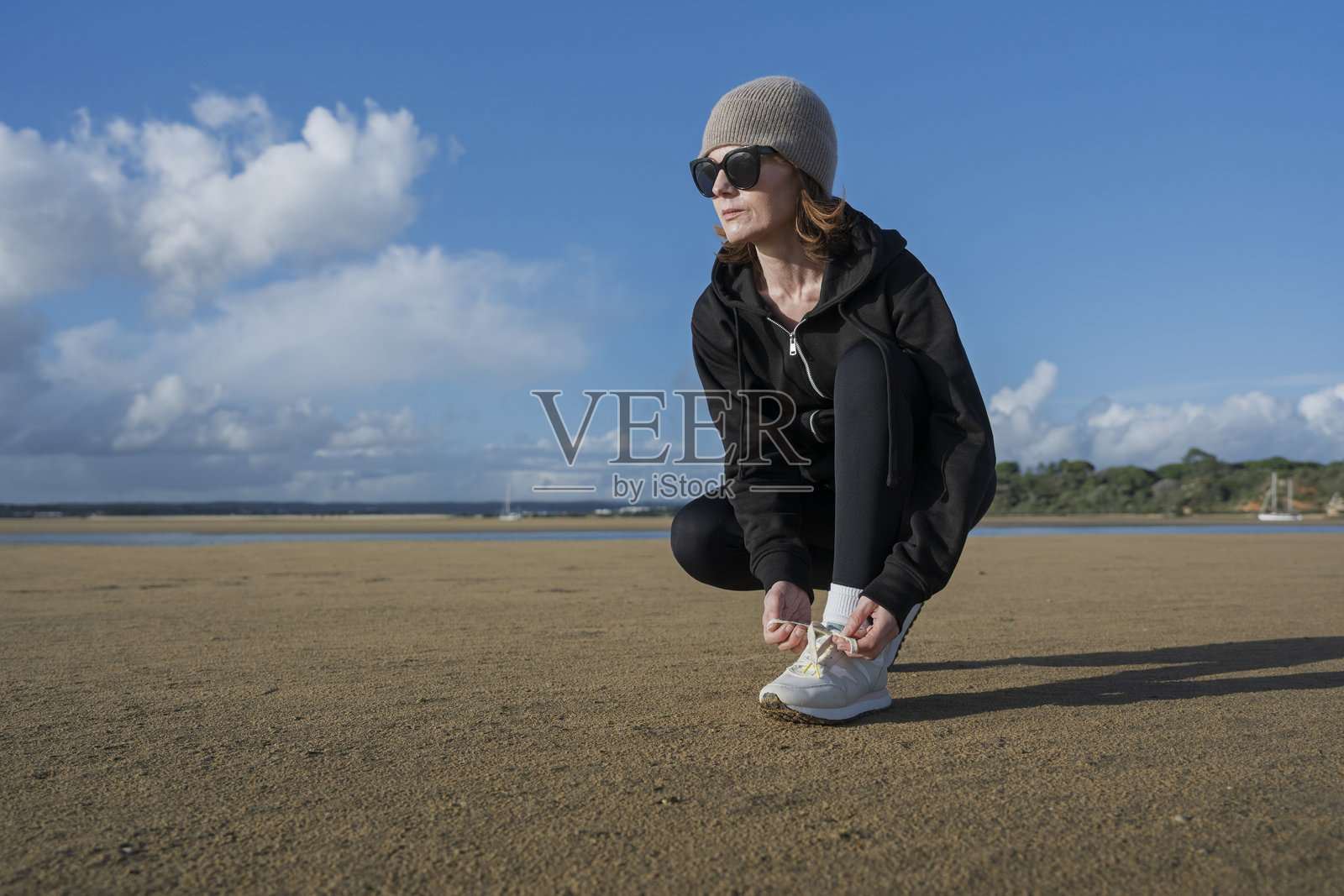 运动风的女性跑者在海滩训练，系着鞋带照片摄影图片