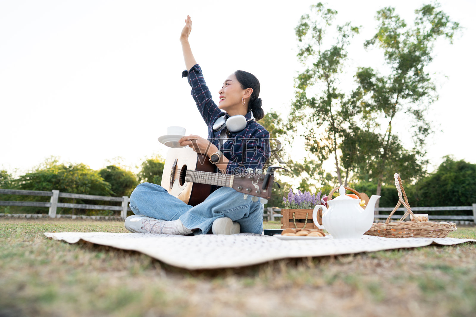 夕阳下，快乐的亚洲女性在公园的野餐垫上弹奏木吉他放松，生活方式与音乐爱好理念照片摄影图片