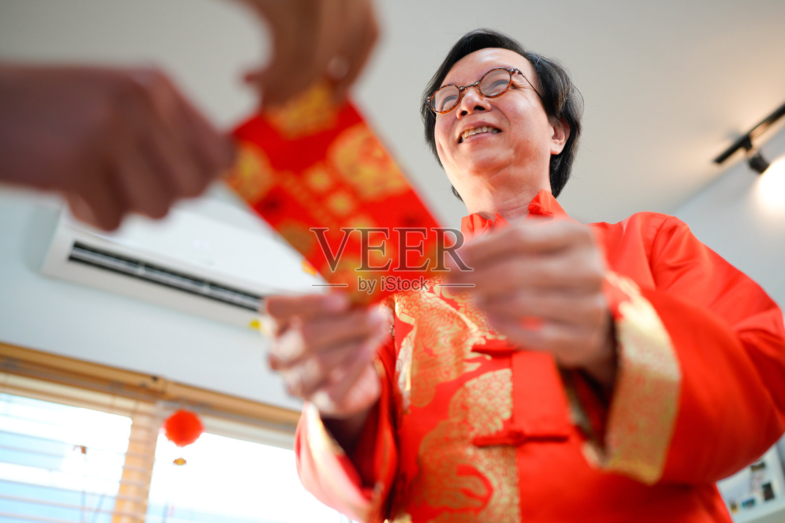 一位身着传统服饰的中国老年男士，在中国新年室内庆祝活动中，高兴地将红包递给他的成年女儿或亲戚。照片摄影图片