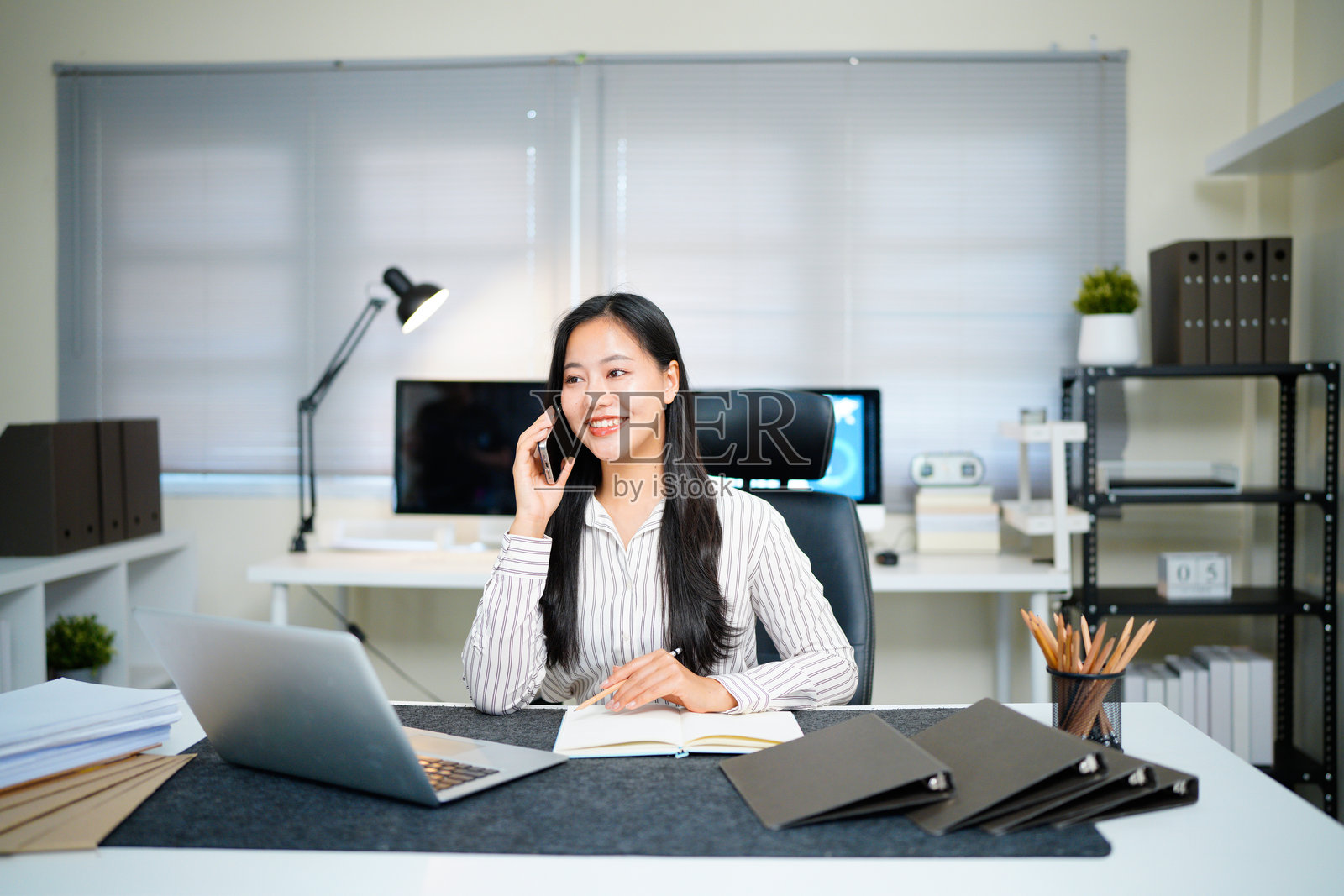 一位年轻迷人的亚洲女商人，面带微笑，正在办公室里用手机交谈。照片摄影图片