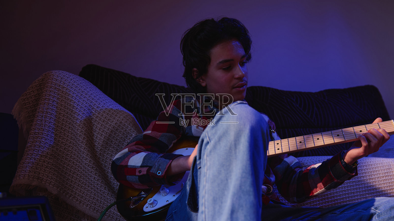 青少年在家中弹奏电吉他，背景有蓝色和橙色灯光照片摄影图片