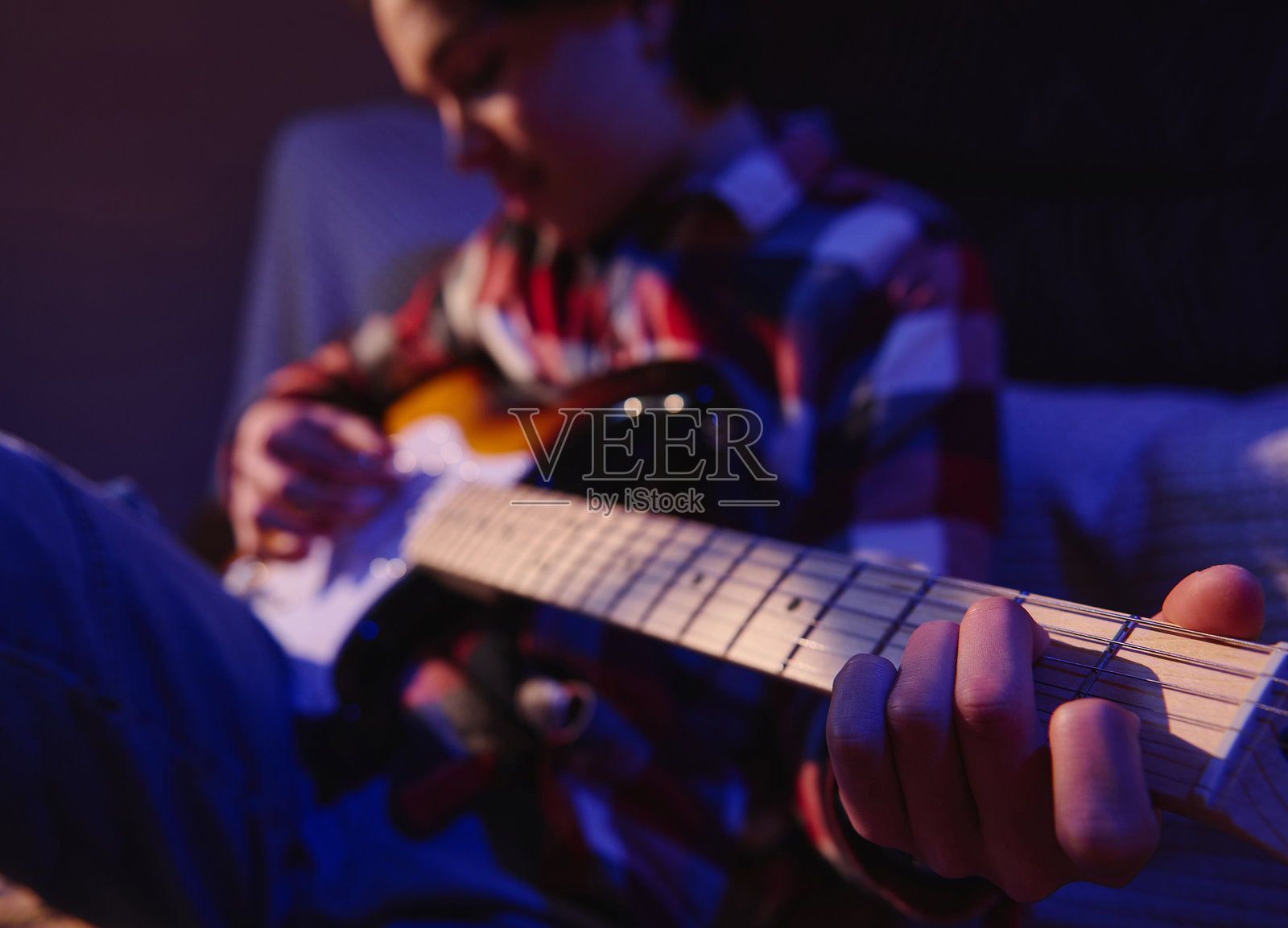 一名少年在家中弹奏电吉他，灯光呈蓝色和橙色，进行随性的音乐练习照片摄影图片