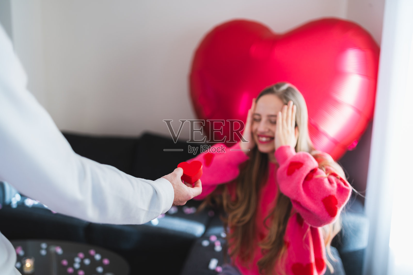 女人在情人节房间里惊喜又开心，男人递上心形礼物照片摄影图片