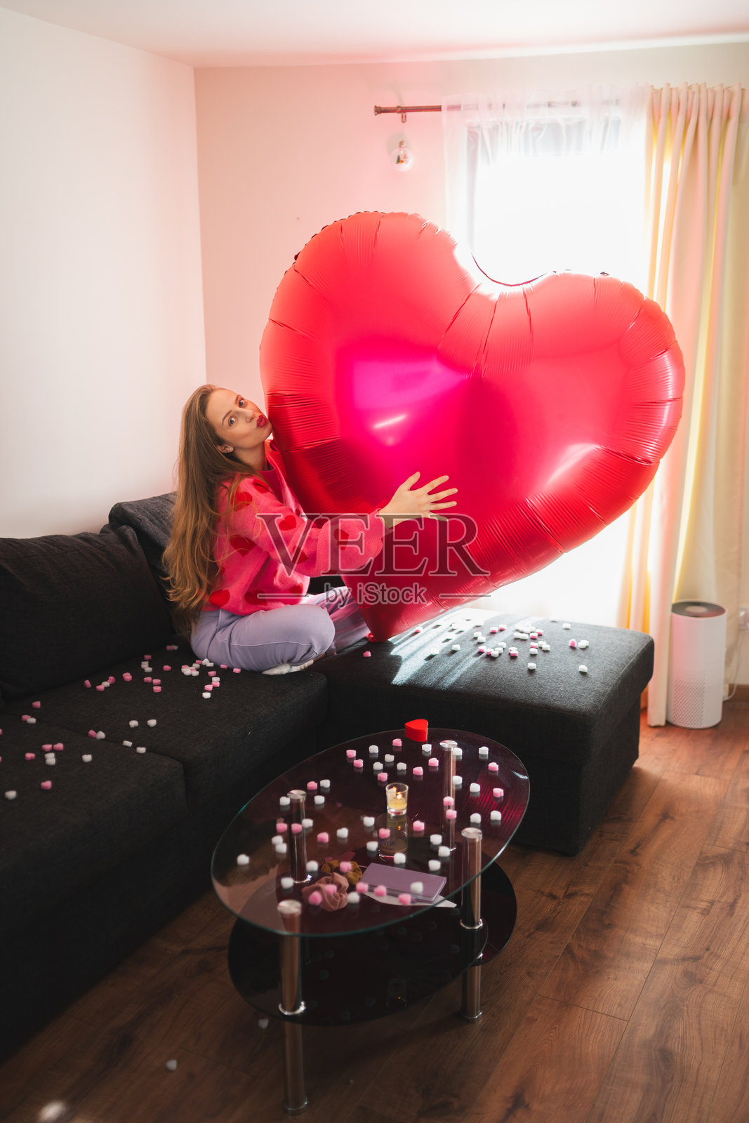 房间里，女人手持一个大心形气球，周围环绕着爱心和蜡烛，营造出俏皮的情人节场景照片摄影图片