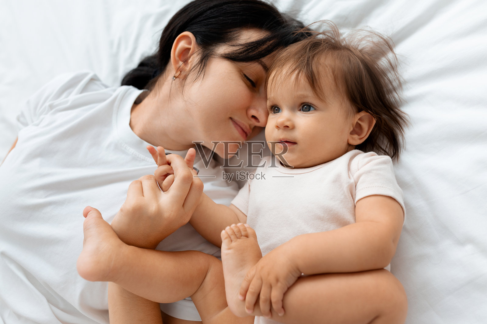 母亲在家中床上与婴儿依偎而卧照片摄影图片