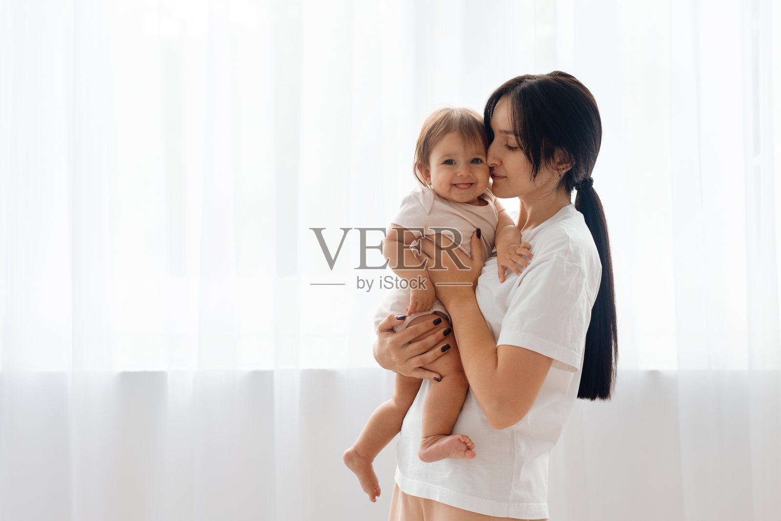 一位高加索母亲在室内抱着微笑的婴儿。居家生活写实肖像。照片摄影图片