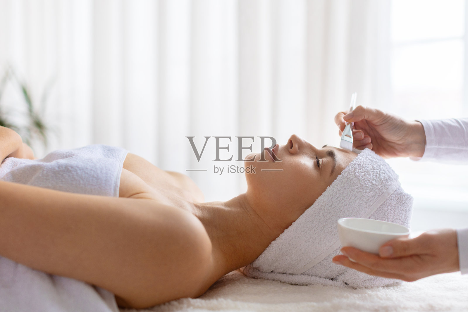 理疗师在水疗中心用刷子给放松的女士敷上化妆泥面膜照片摄影图片