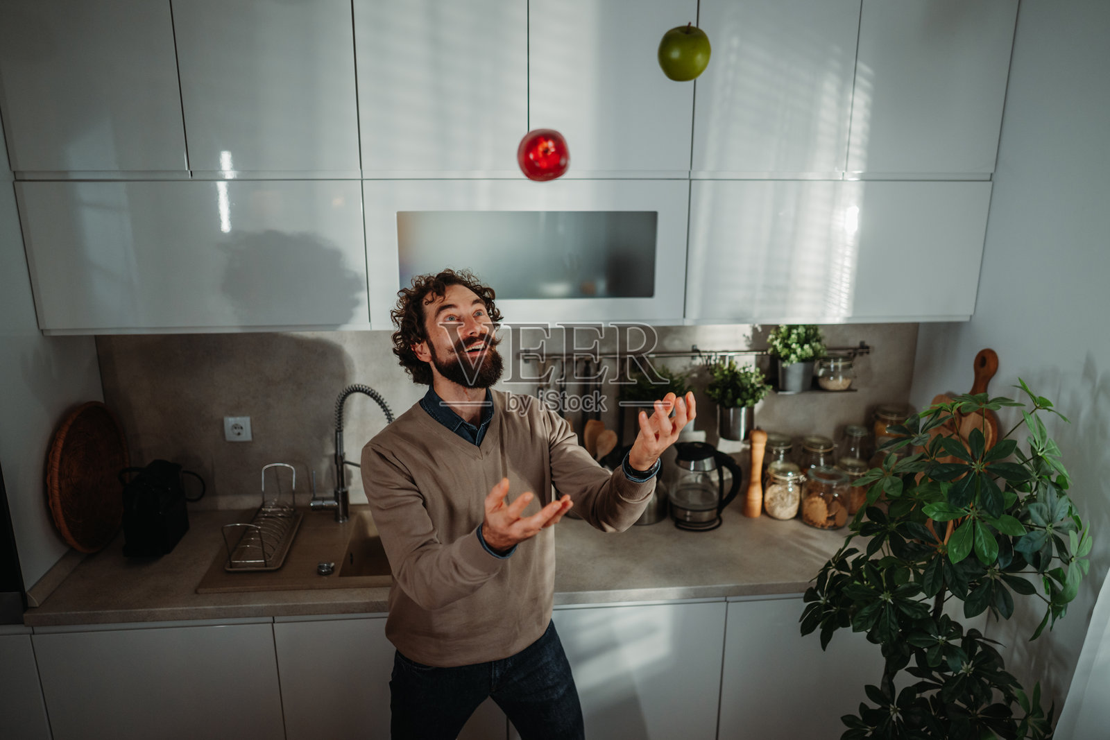 快乐的男人在明亮的厨房里玩苹果杂耍照片摄影图片