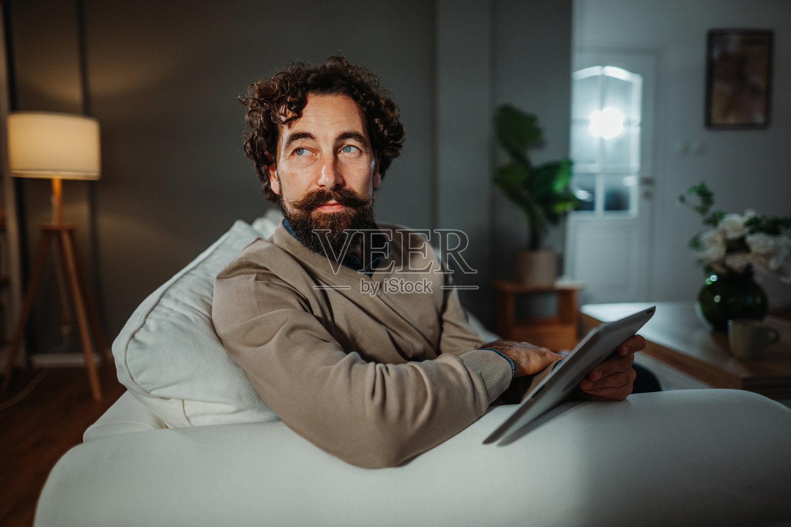 留着胡子的男人坐在客厅里，手持平板电脑若有所思照片摄影图片