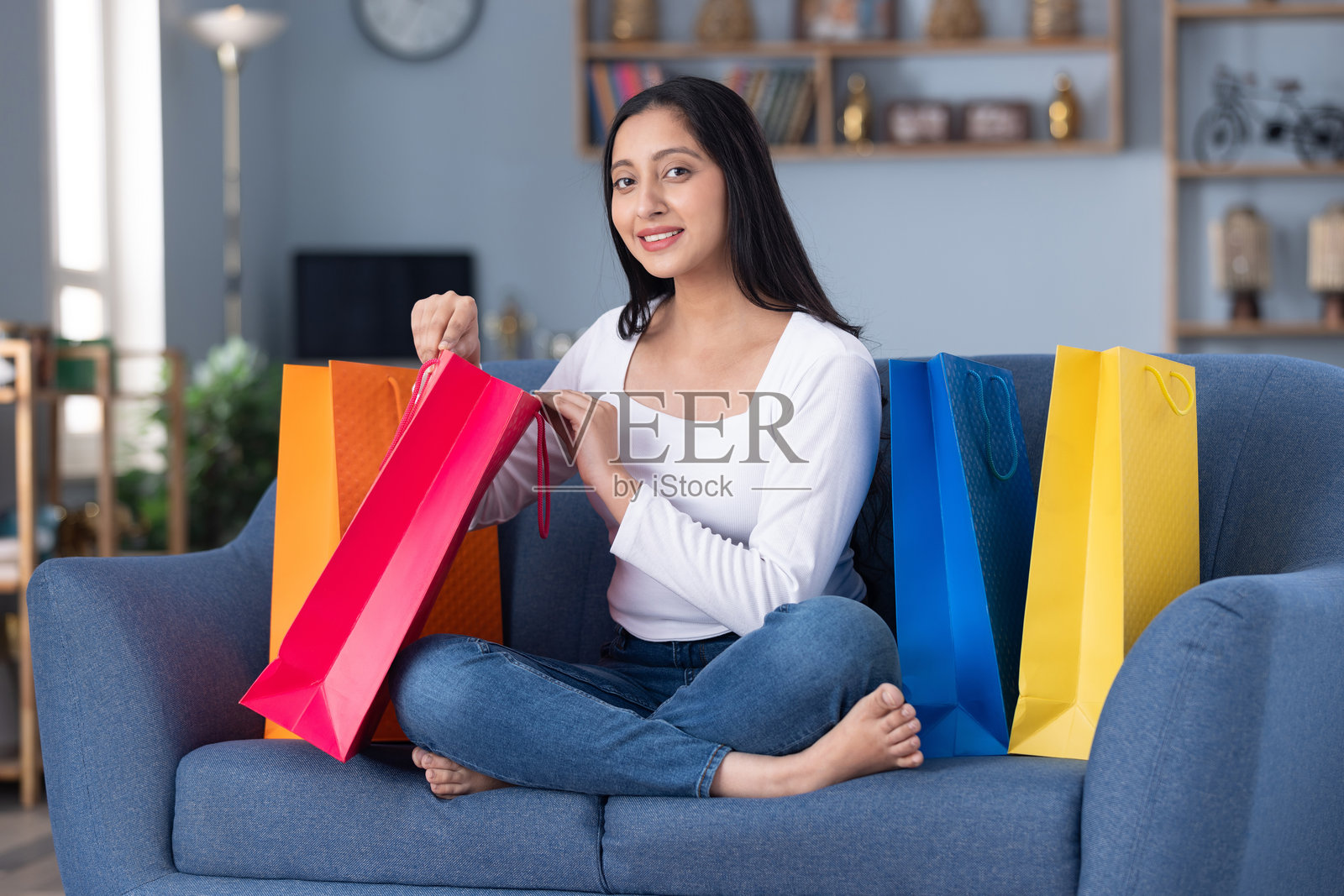 漂亮的年轻女孩坐在家里的沙发上，手里拿着购物袋照片摄影图片