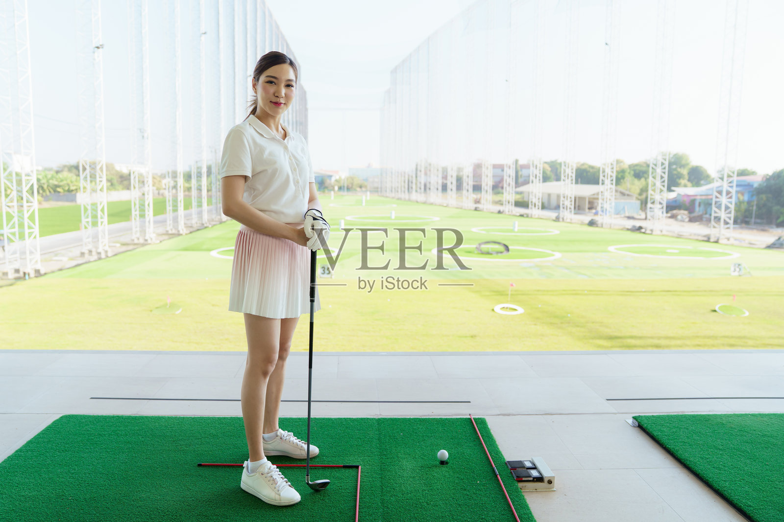 一位女高尔夫球手自信地站在高尔夫练习场，手持高尔夫球杆。照片摄影图片