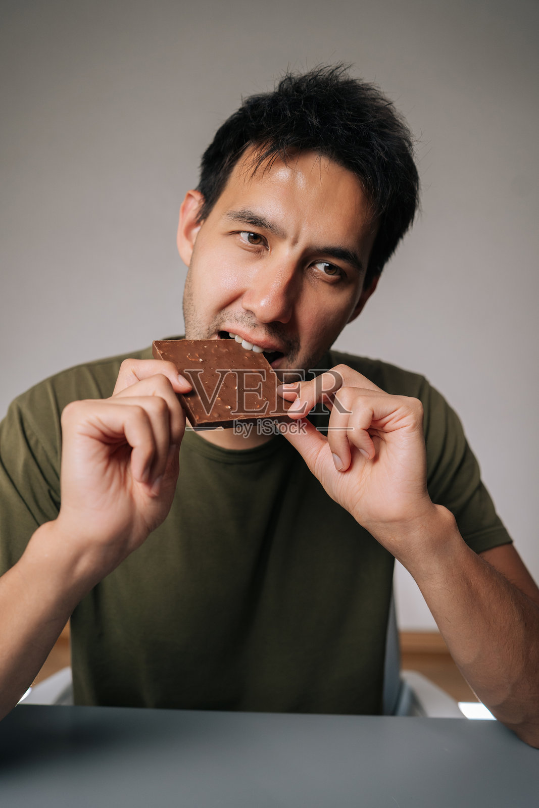 一名快乐的高加索男子坐在桌边，享受着黑巧克力浓郁的美味，在咬下一口令人满意的美味巧克力棒时，脸上洋溢着幸福的享受。照片摄影图片