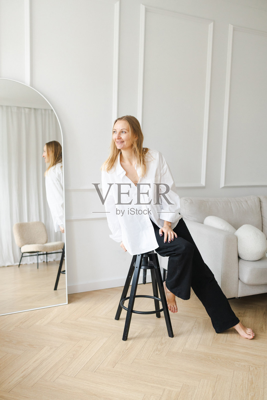 身着白衬衫的优雅女士坐在明亮简约风格的室内，旁边有镜子照片摄影图片