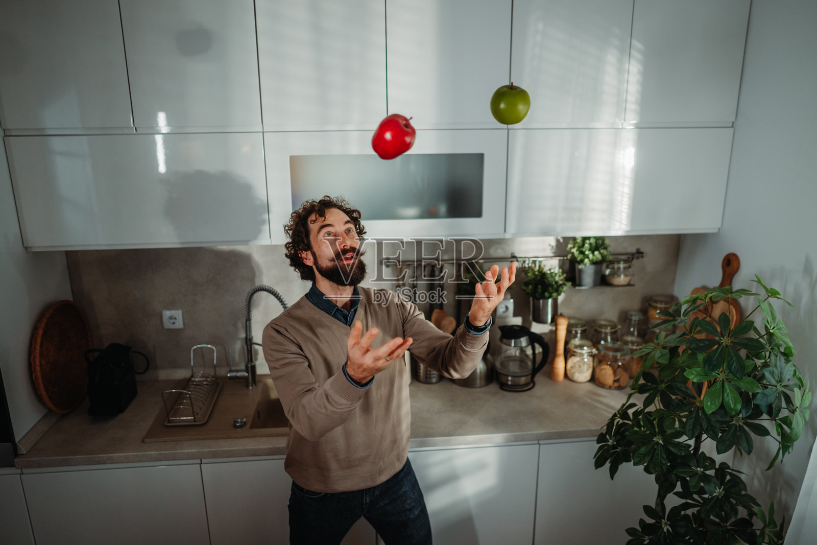 男人在厨房里玩弄红苹果和绿苹果照片摄影图片