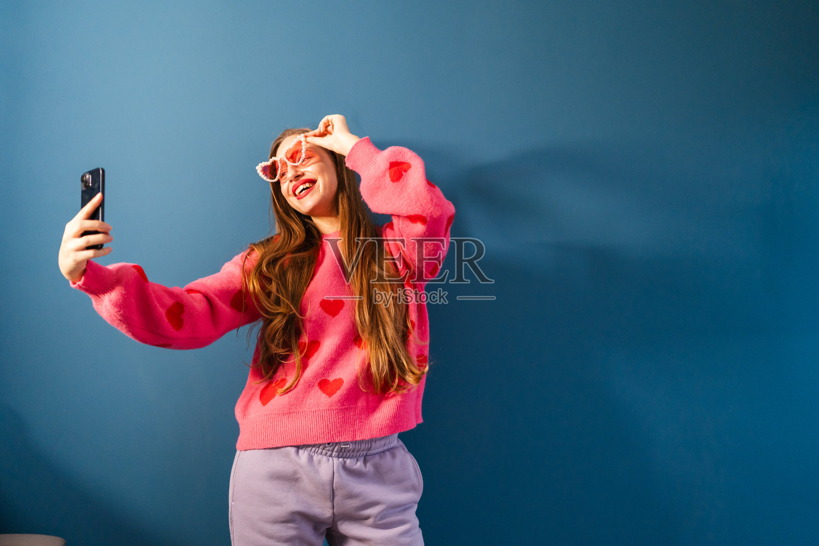 玩趣情人节生活方式概念：戴着心形太阳镜的女人自拍照片摄影图片