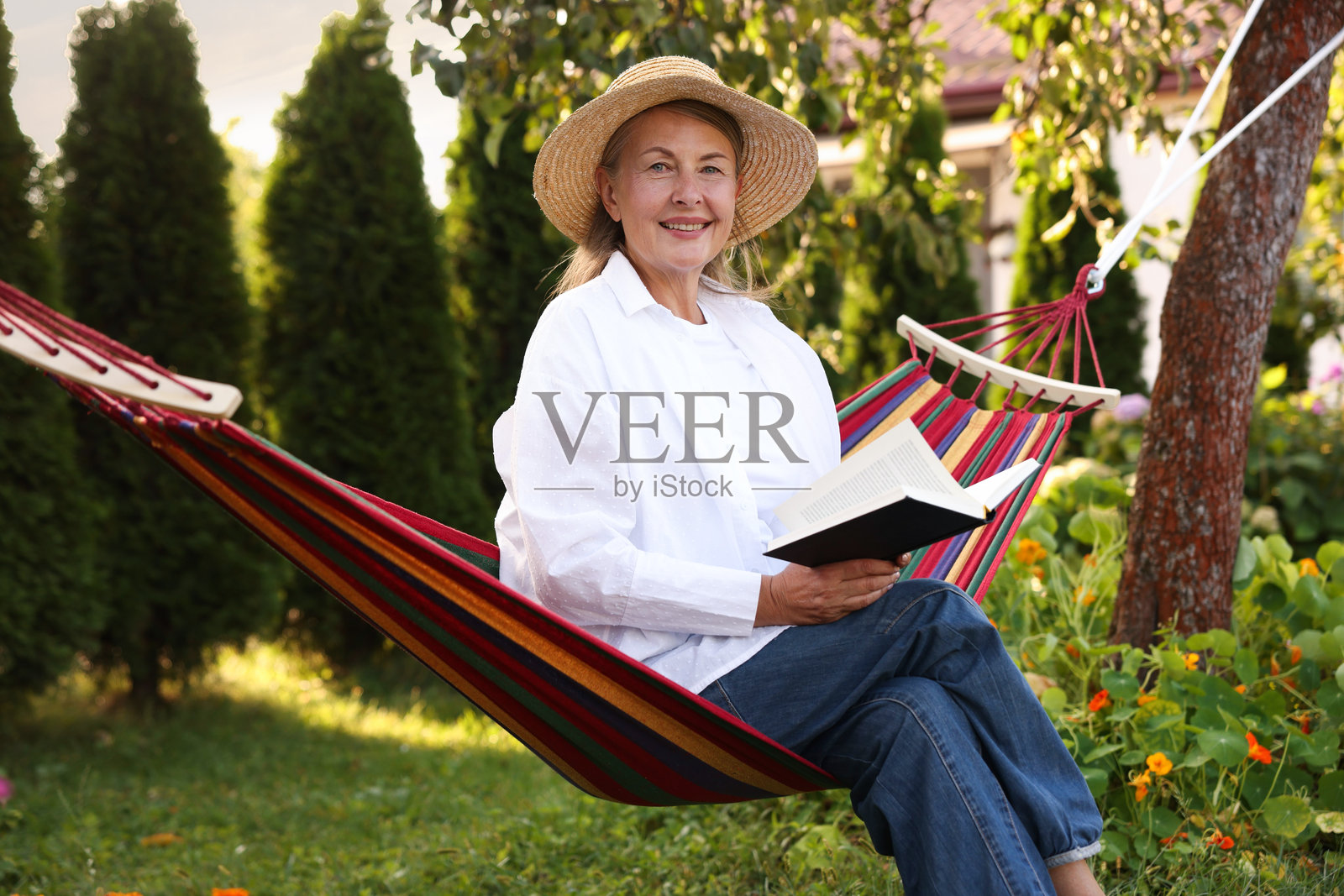 戴草帽的年长女性在户外吊床上读书放松照片摄影图片