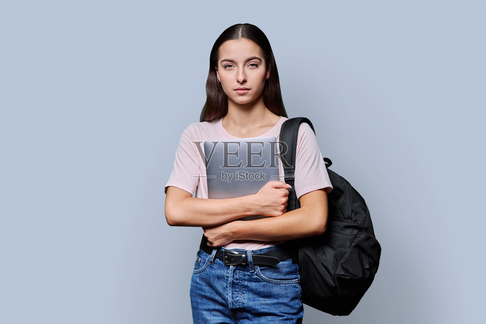 背着背包、带着笔记本电脑的漂亮女高中生肖像，背景为灰色照片摄影图片