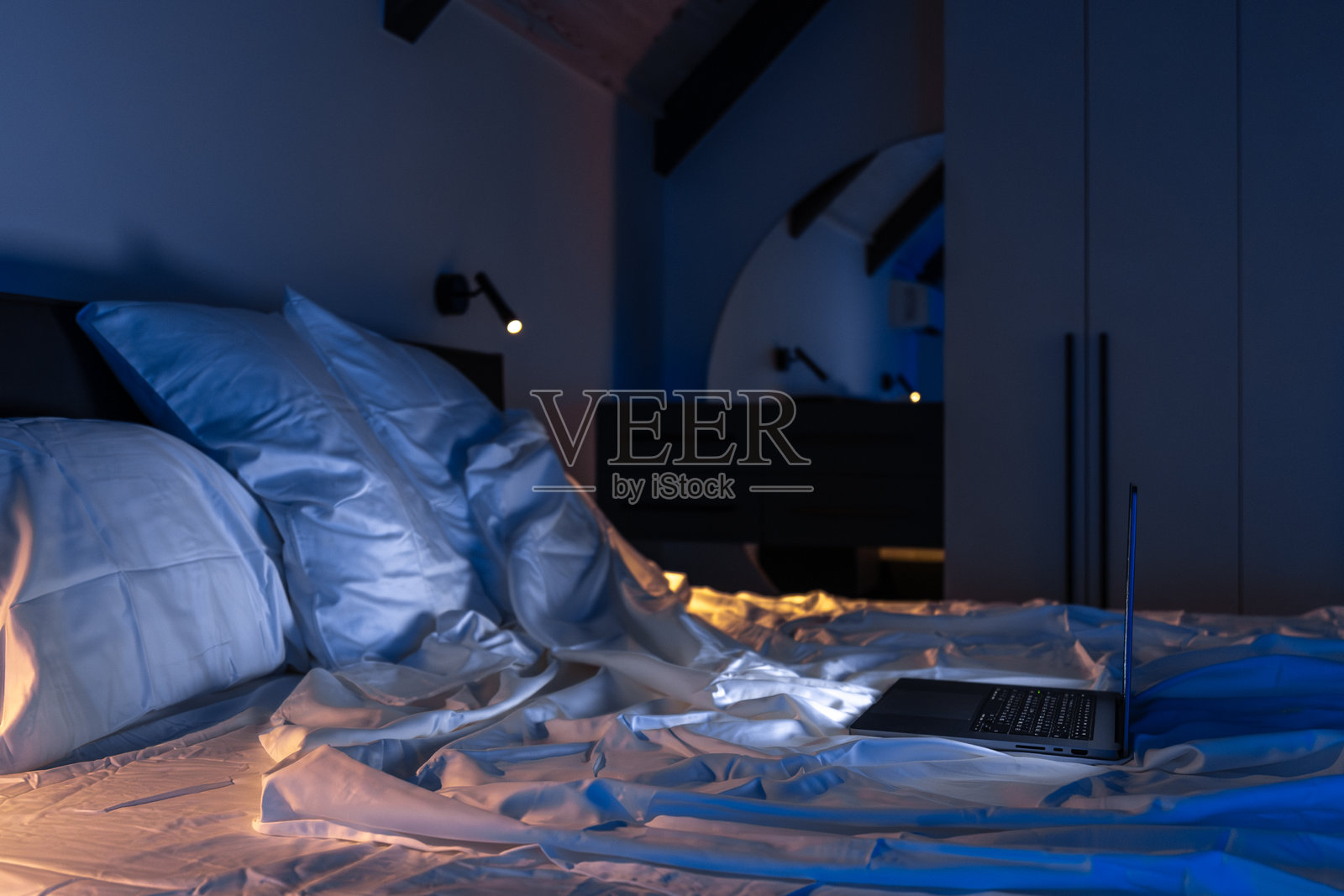 蓝色的阁楼室内，床上放着一台笔记本电脑。宁静的夜晚。照片摄影图片