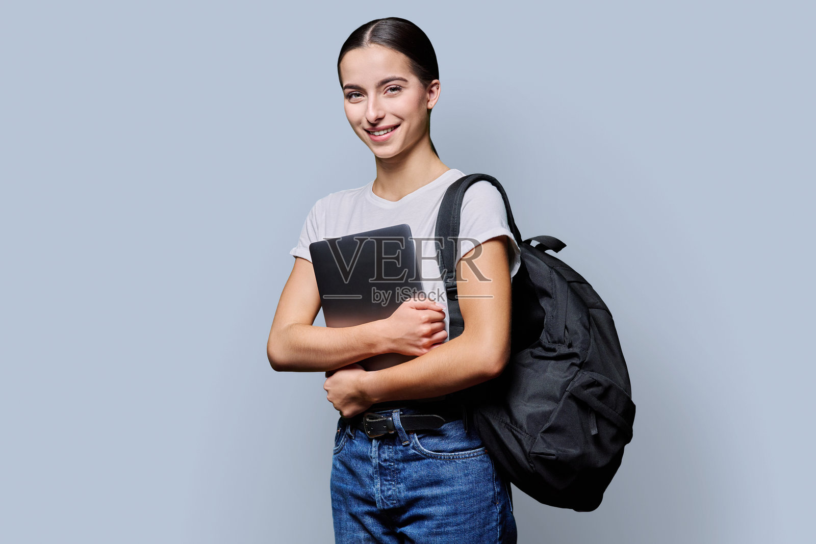 漂亮的十几岁女学生肖像，背着背包，带着笔记本电脑，背景为灰色照片摄影图片