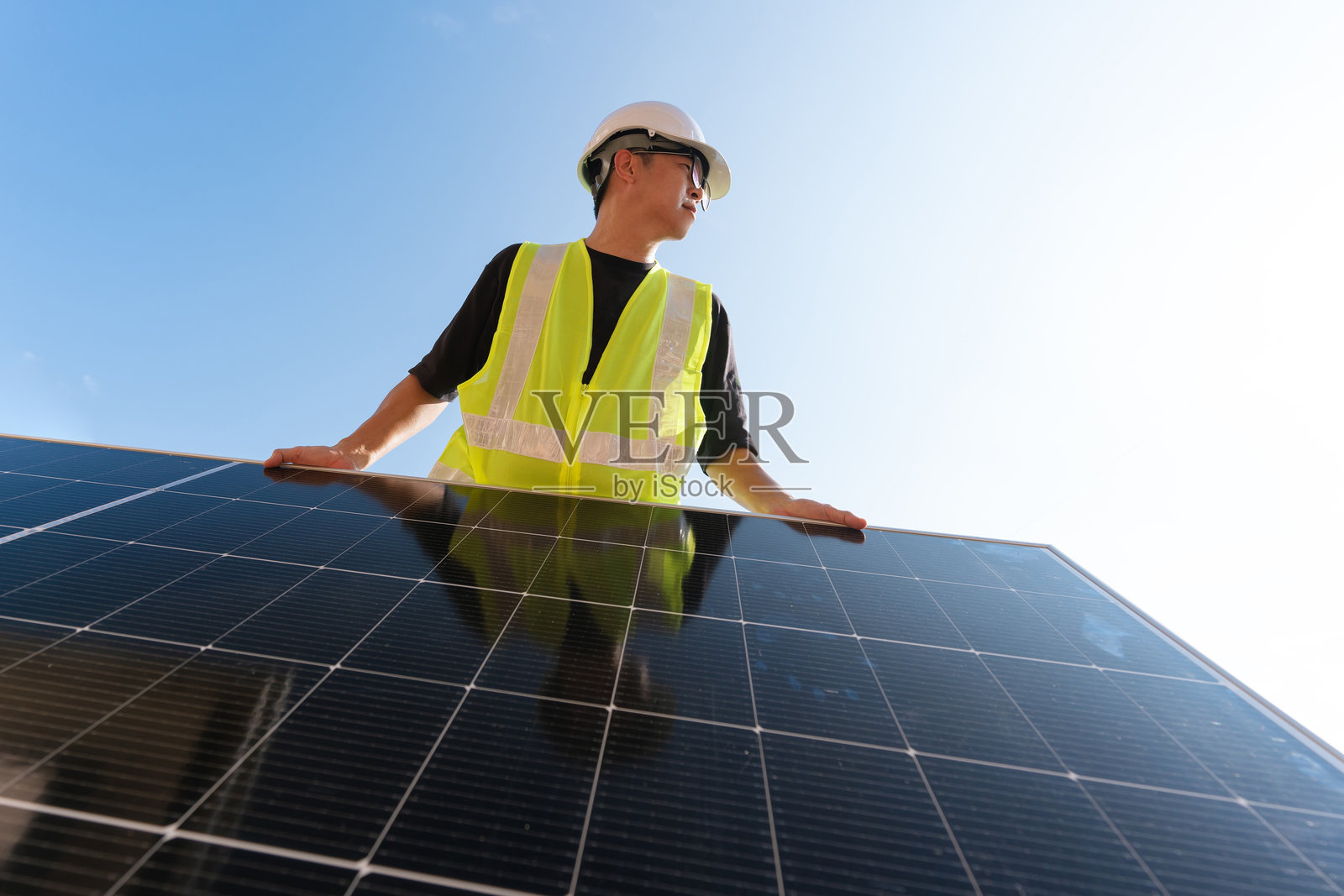 一名穿着安全背心和安全帽的男工程师在明亮的阳光下拿着太阳能电池板开始安装。照片摄影图片