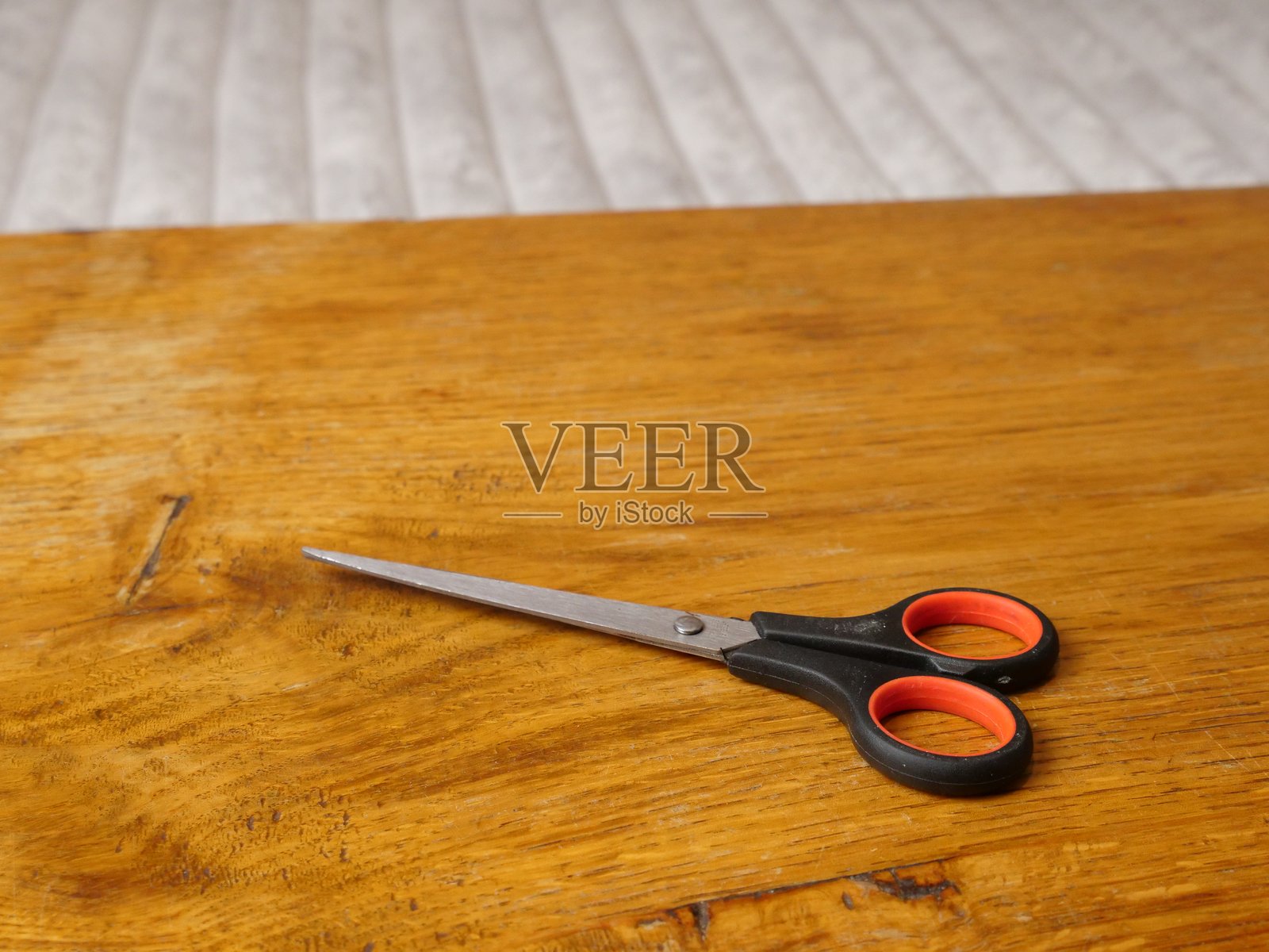 一把黑色手柄的家用剪刀放在一张磨损的木桌表面上。照片摄影图片