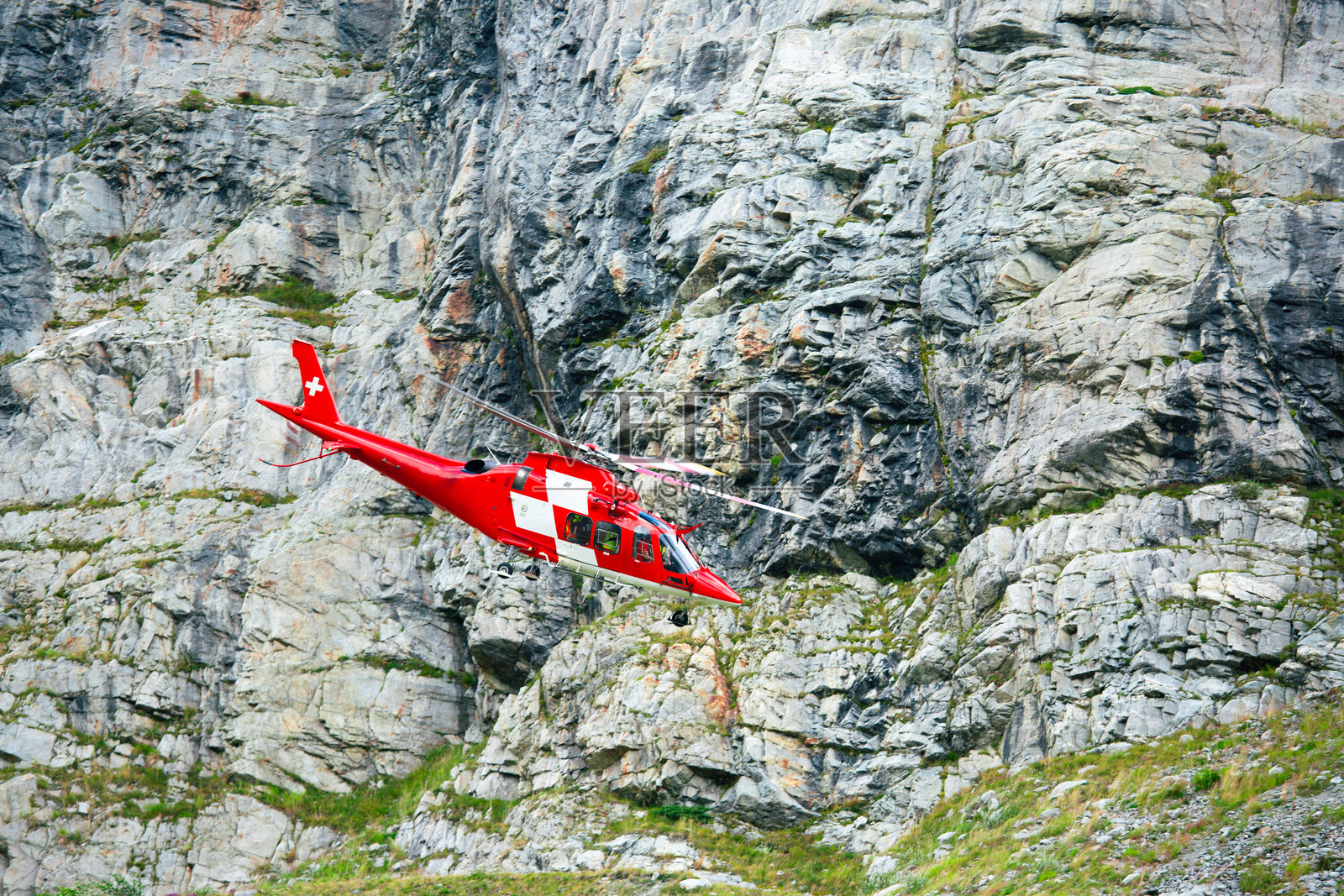 红色的救援直升机沿着陡峭的岩石山壁飞行照片摄影图片