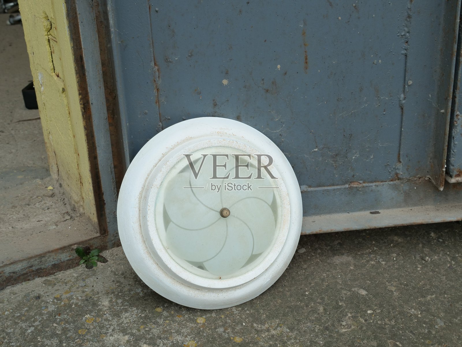 磨砂玻璃圆形吸顶灯灯具，放置在靠近金属门的混凝土地板上。照片摄影图片