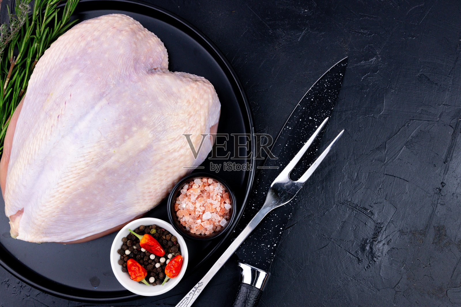 黑色盘子里的新鲜火鸡胸肉，配有香料和厨具，准备烹饪和制作餐点照片摄影图片