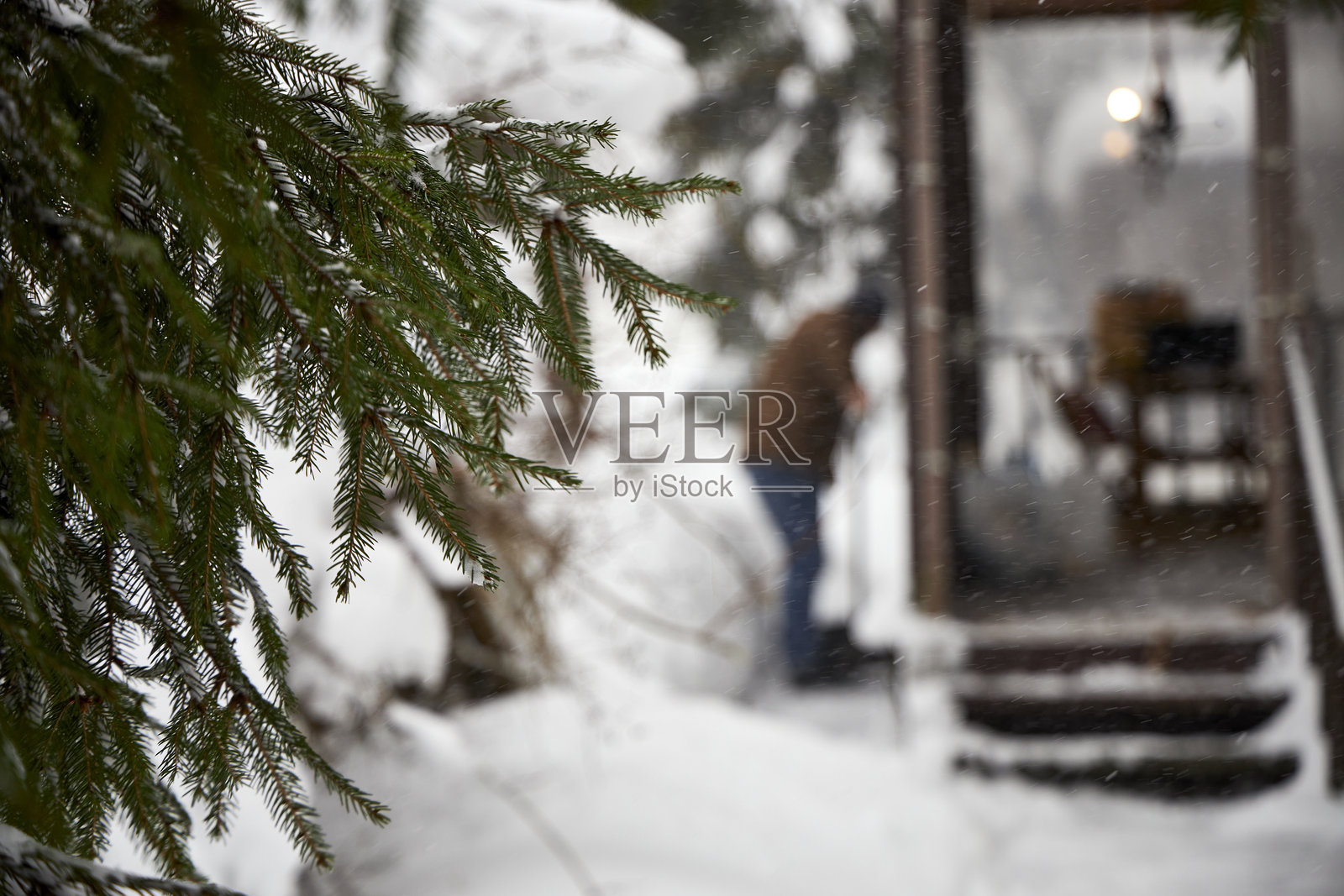 暴风雪过后，一名男子正在一所房子附近铲除厚厚的积雪。季节性的户外活动、冬季维护、暴风雪后的除雪、寒冷天气生活方式和极端冬季条件照片摄影图片