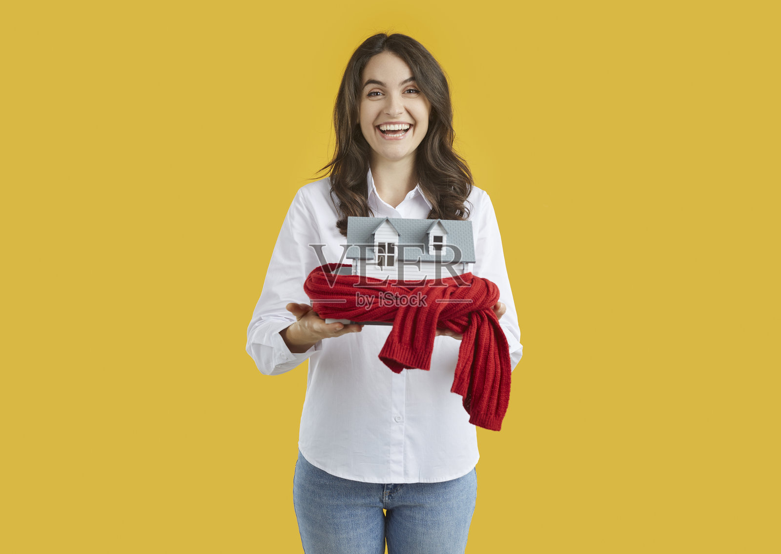 一位女士抱着被温暖围巾包裹的玩具房屋，象征着供暖系统或寒冷多雪的冬天。照片摄影图片