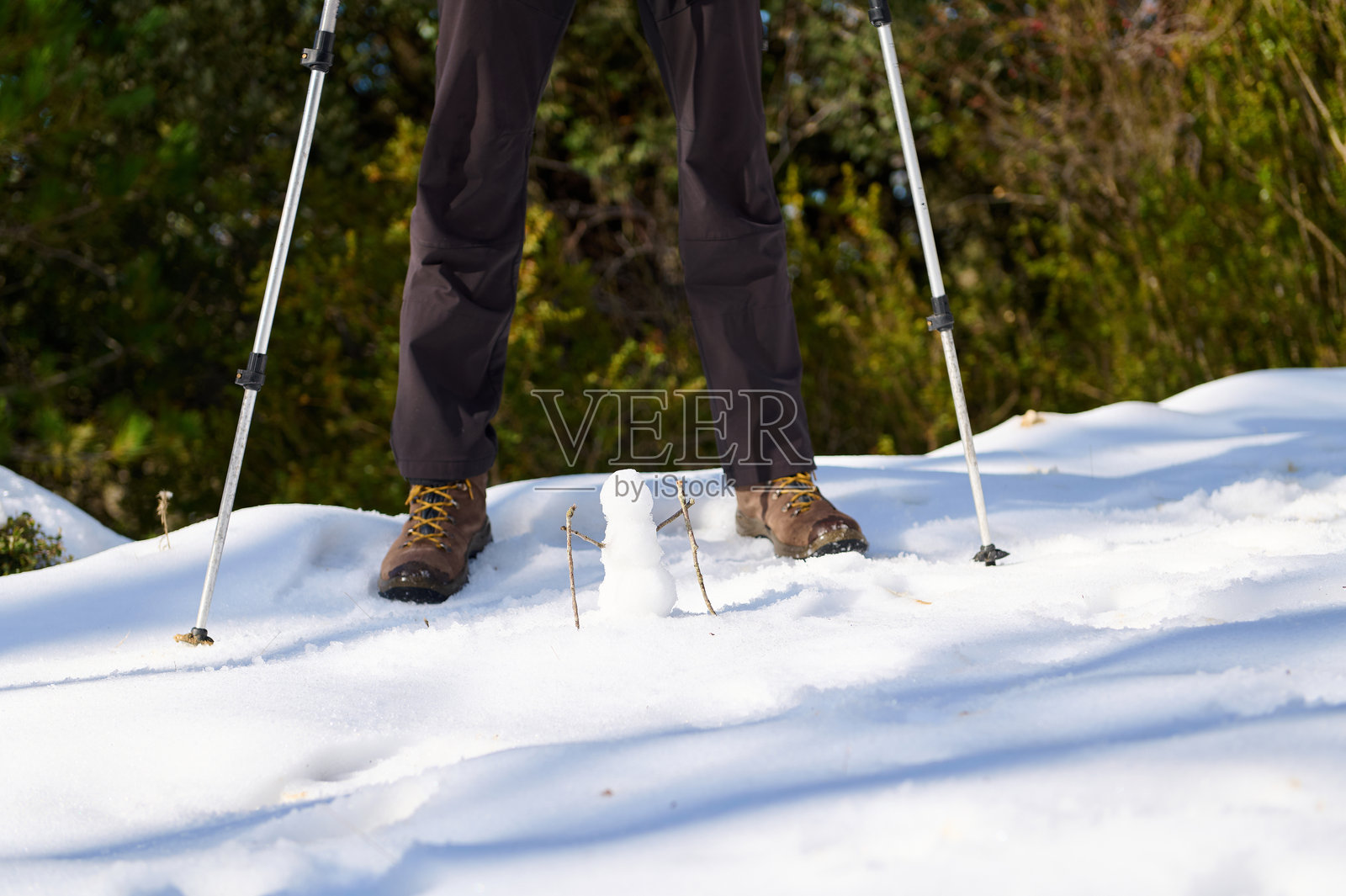 徒步者在冬季森林的雪地小径上，手持登山杖，旁边还有一个小雪人照片摄影图片