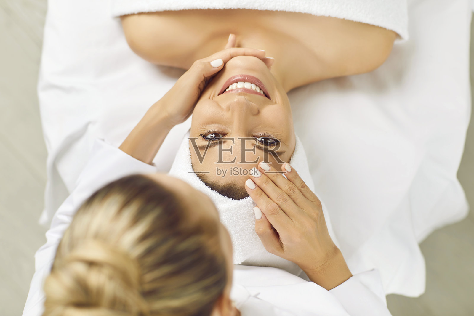 水疗沙龙里，一位快乐的女士正看向镜头，接受美容师的美容护理。照片摄影图片