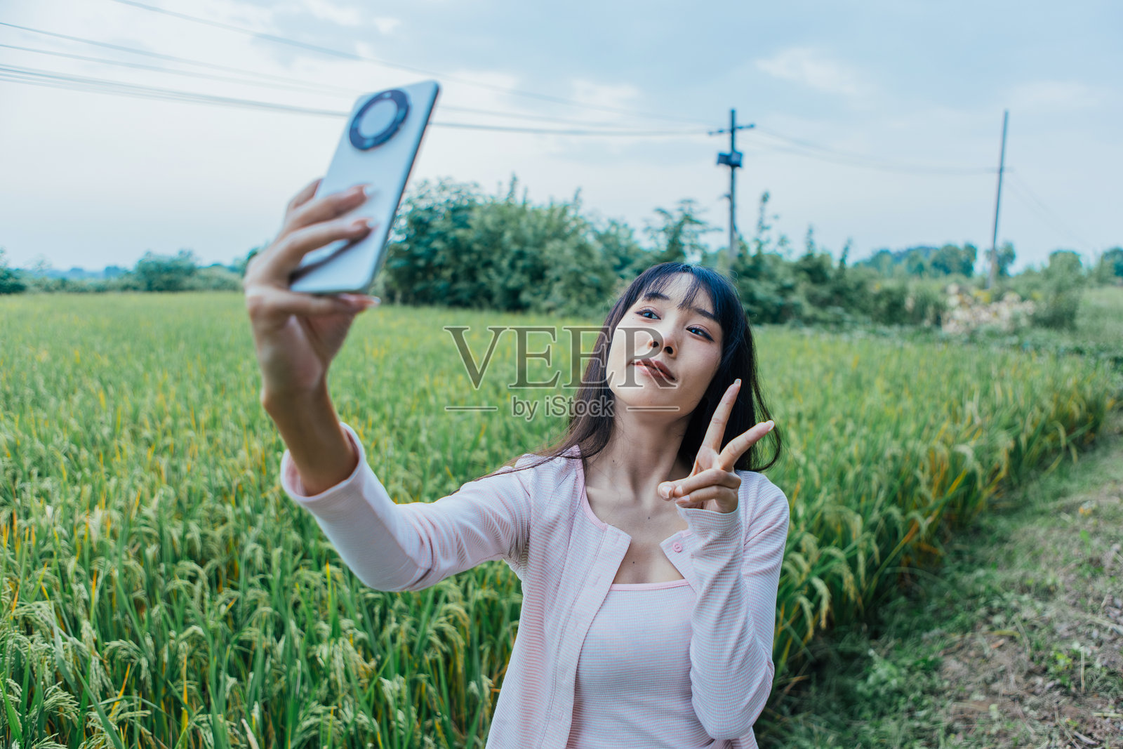 年轻的亚洲女性在乡村道路上用智能手机自拍，享受乡村旅行，同时连接社交媒体，展现现代数字生活方式。照片摄影图片