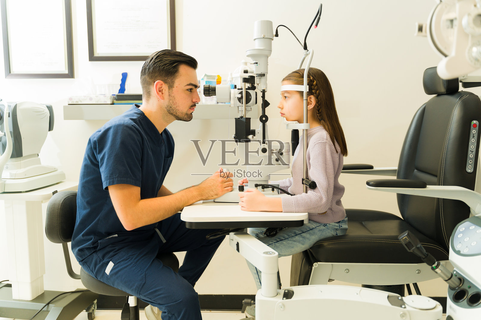 一名眼科医生在现代诊所使用裂隙灯检查小女孩视力，进行眼部健康检查的侧面视图照片摄影图片