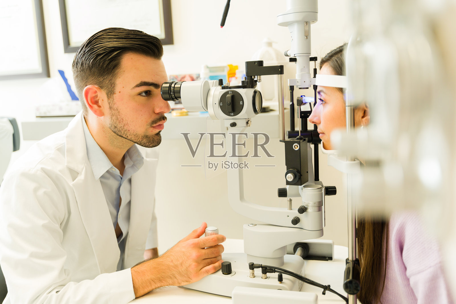 一位西班牙裔眼科医生在诊所为病人进行全面的眼部健康检查时，使用裂隙灯检查病人的视力照片摄影图片