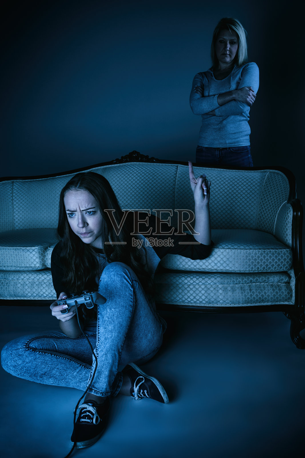 少女玩电子游戏，母亲在一旁不满地看着照片摄影图片