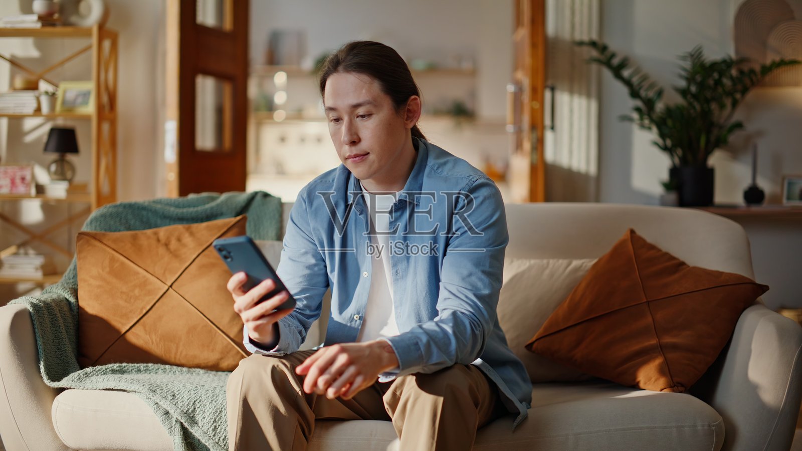 沙发上，一位兴奋的时尚青年近距离看着手机屏幕，为在线获胜而欢呼照片摄影图片