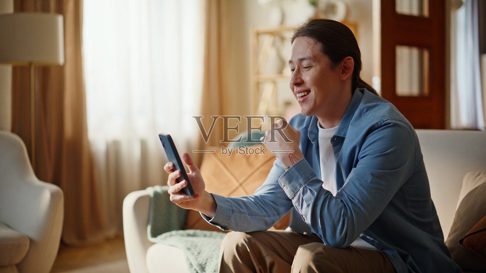 快乐的博主在现代客厅里用智能手机直播，是一位积极的男性意见领袖照片摄影图片