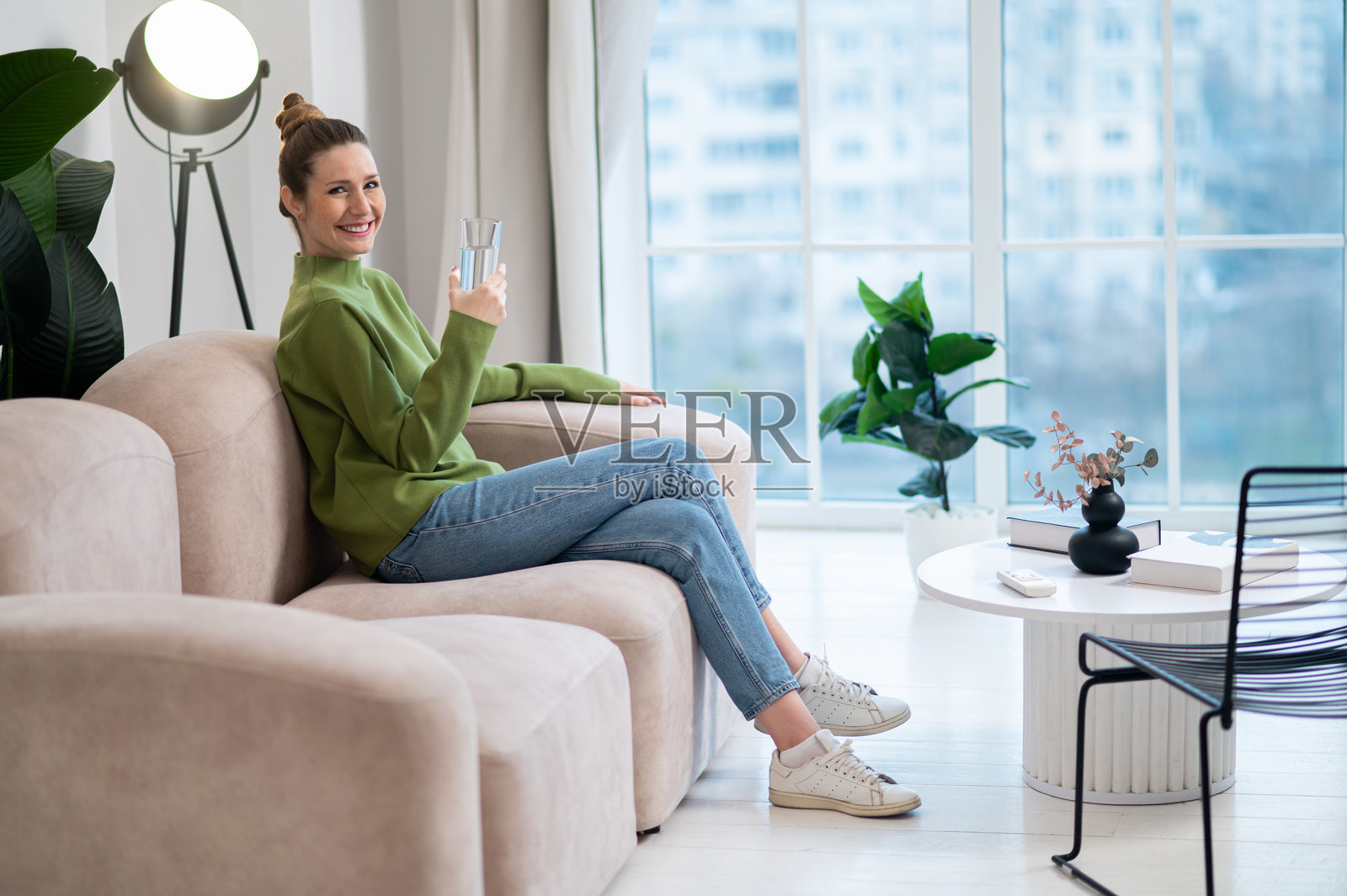 年轻女子身穿绿色衣服，坐在沙发上喝水照片摄影图片