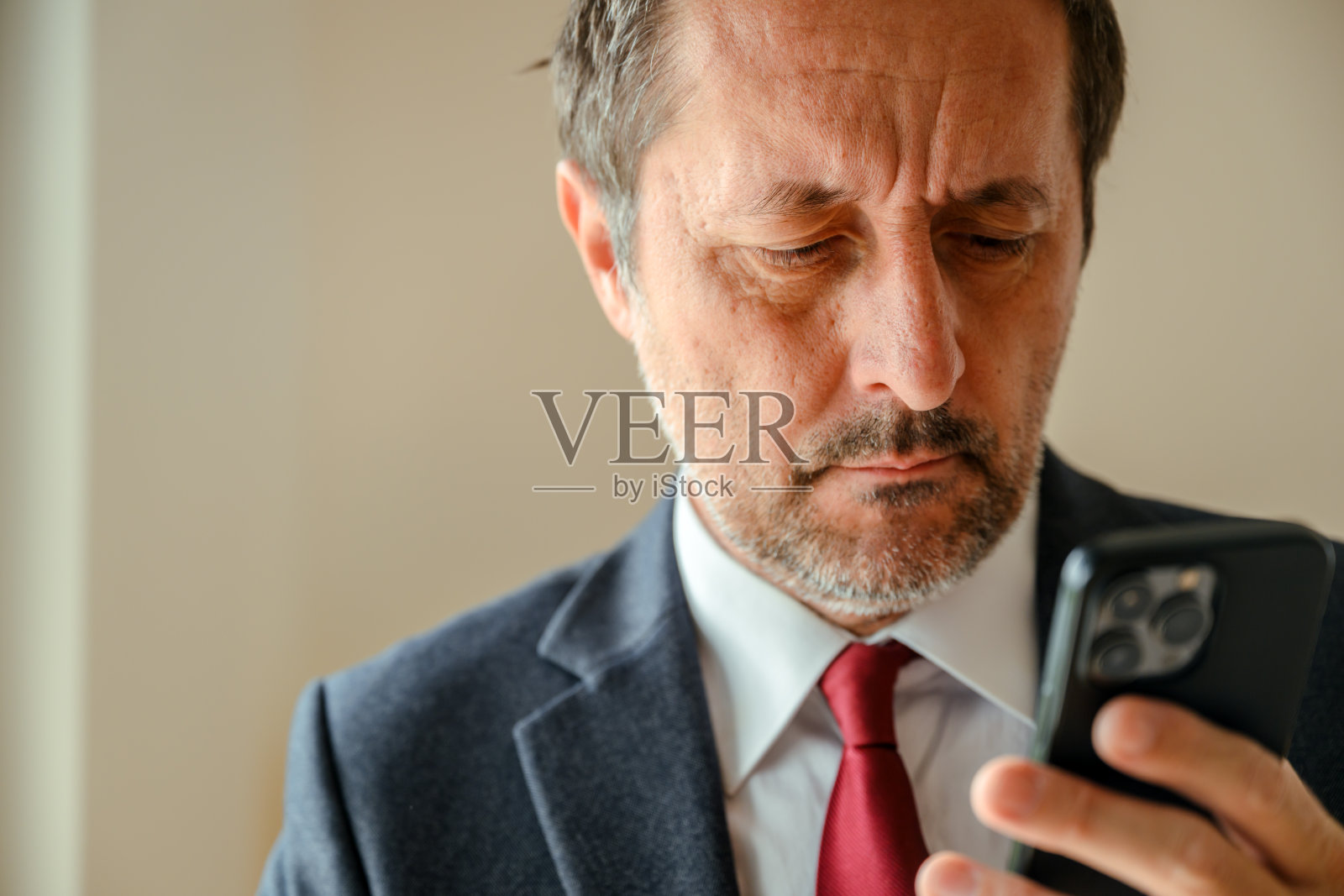 成熟的CEO商人肖像，在明亮的现代办公室里看着智能手机屏幕。照片摄影图片