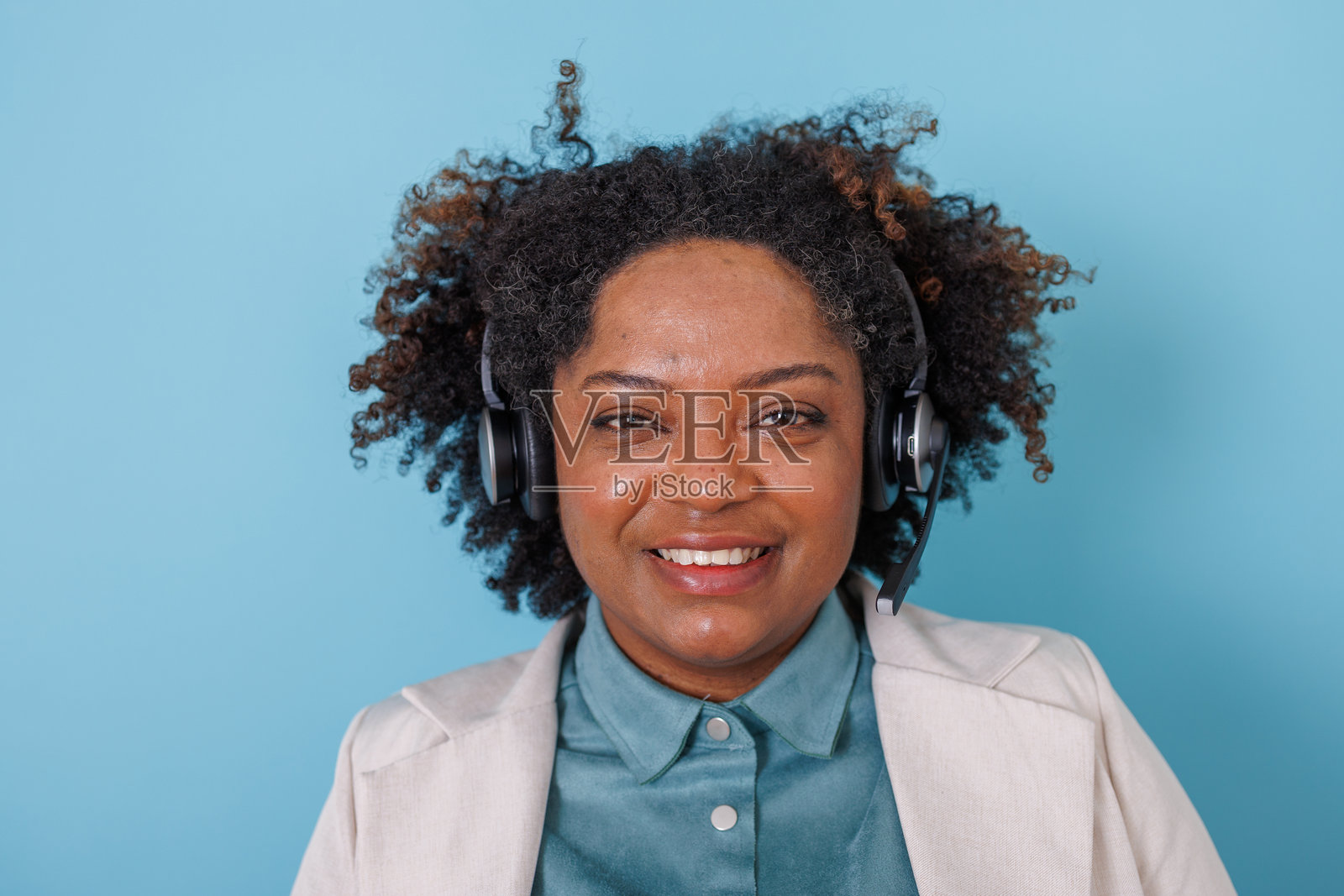 一位戴着耳机的黑人女性，身着商务休闲装，面带微笑，在蓝色背景前提供友好的客户服务照片摄影图片