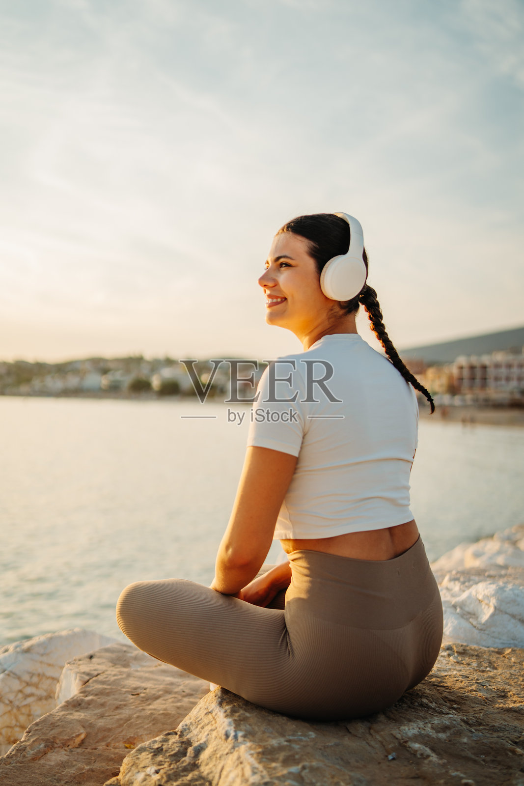 年轻女子在日落时分戴着耳机在海边享受音乐照片摄影图片
