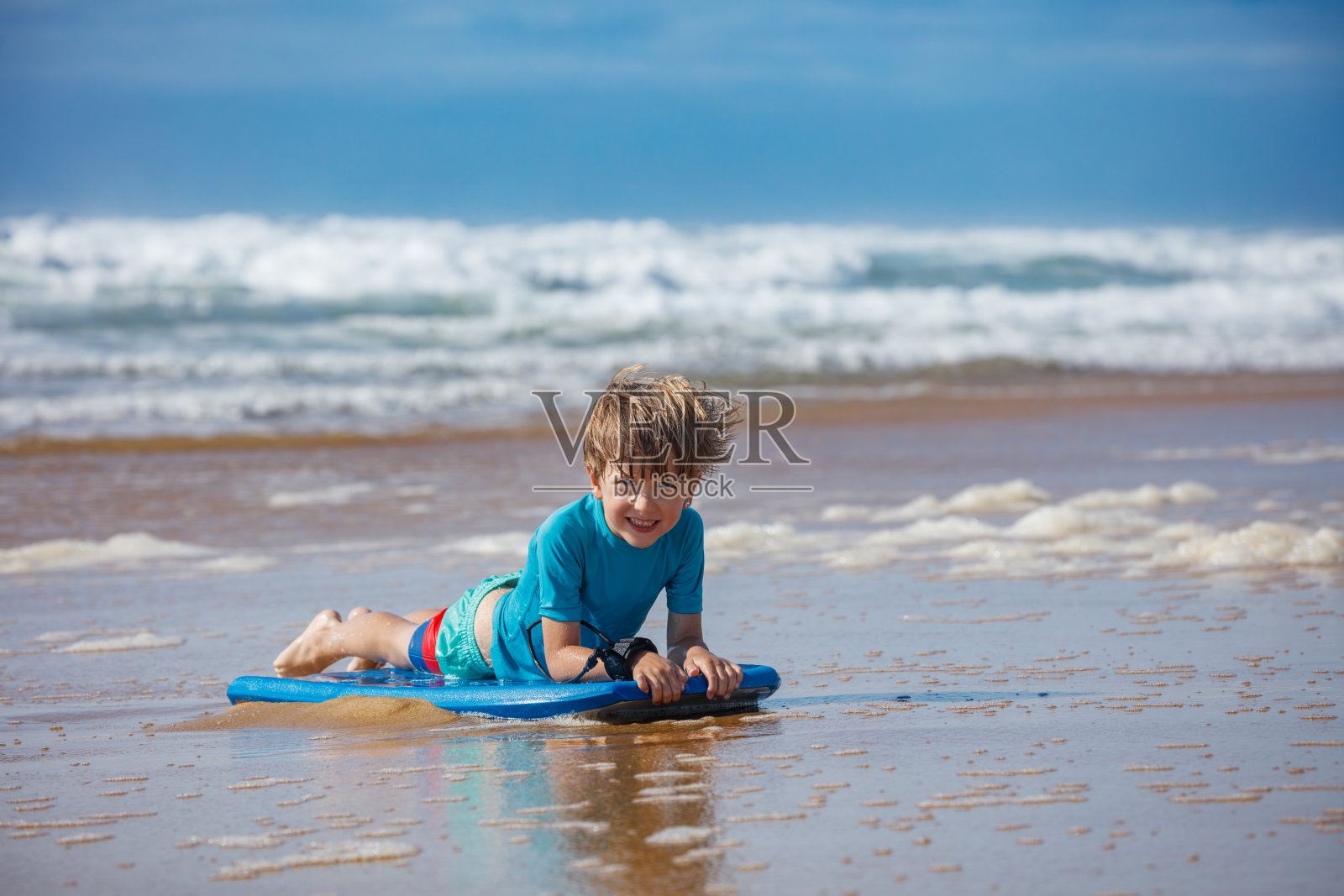 男孩在阳光明媚的海滩边开心地玩趴板冲浪，享受假期照片摄影图片