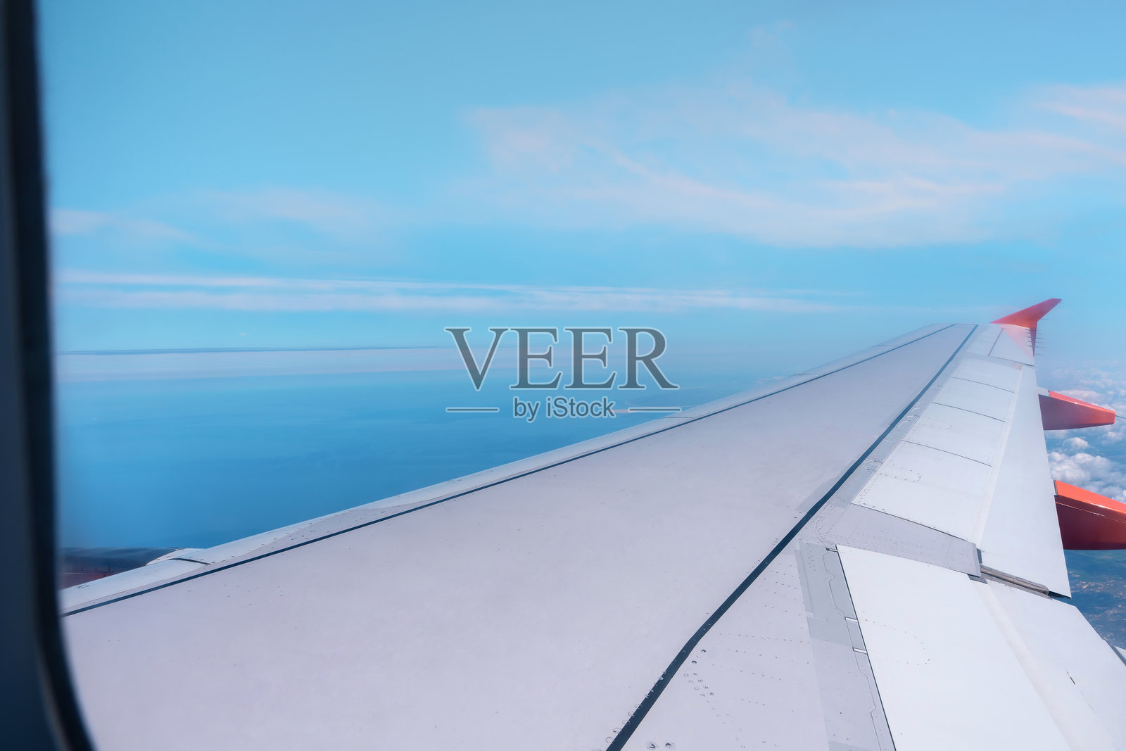 View from airplane window during flight over ocean with clear blue sky and distant clouds照片摄影图片