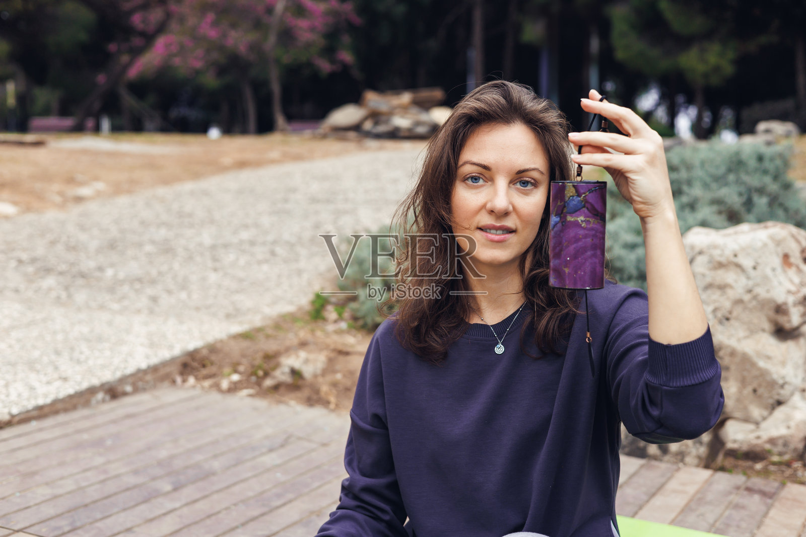一位棕色头发的年轻白人女性坐在湖边，手持铃铛，用于声音疗愈或冥想。照片摄影图片